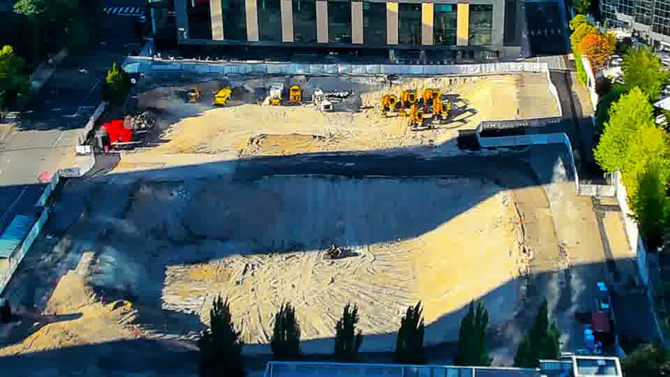 Construction camera frame at 5:30 PM PT. Shadows have lengthened across the site, but the positioning of the machines and materials appears static.