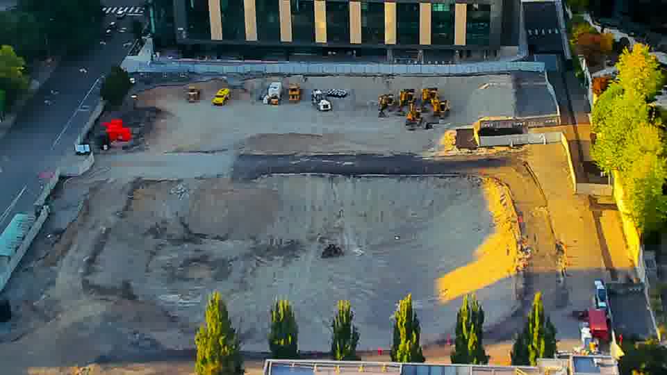 Construction camera frame at 6:45 PM PT. A small, light-colored vehicle has moved from near the center of the site toward the driveway on the left. Otherwise, the equipment and the overall scene look much the same as they did before.