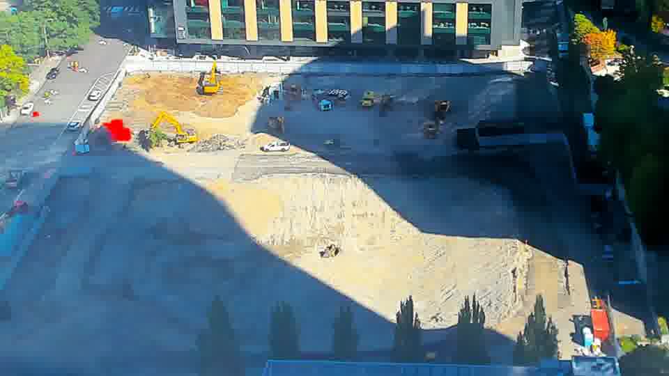 Construction camera frame at 10:45 AM PT. A white vehicle has entered the site via the driveway on the left. Otherwise, no visible change between these frames.