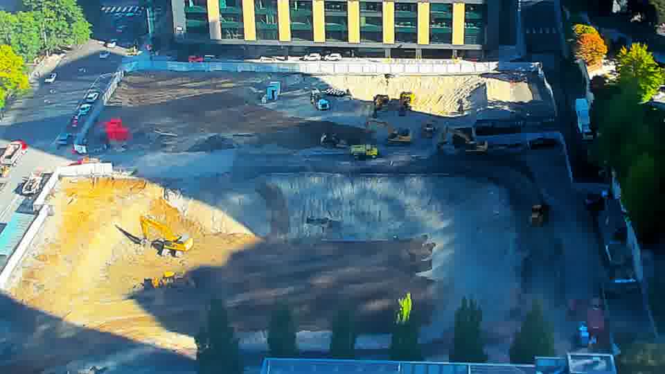 Construction camera frame at 9:45 AM PT. Two people are visible near the center of the site, where there were none before.