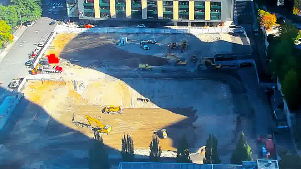Construction camera frame at 10:15 AM PT. A small, red object has appeared near the center of the site, but its nature is unclear.