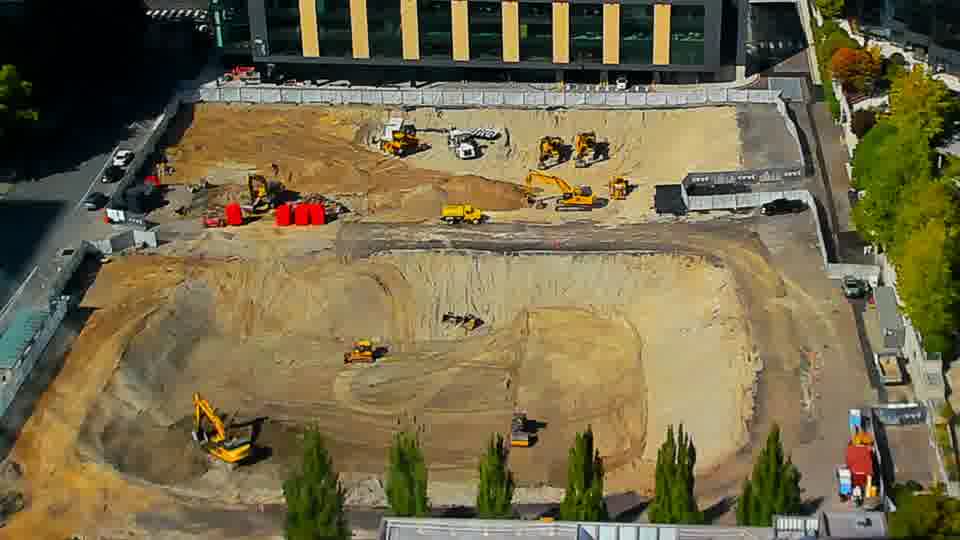 Construction camera frame at 3:15 PM PT. A yellow excavator near the lower-right corner of the site has shifted position slightly. Otherwise, no visible change between these frames.