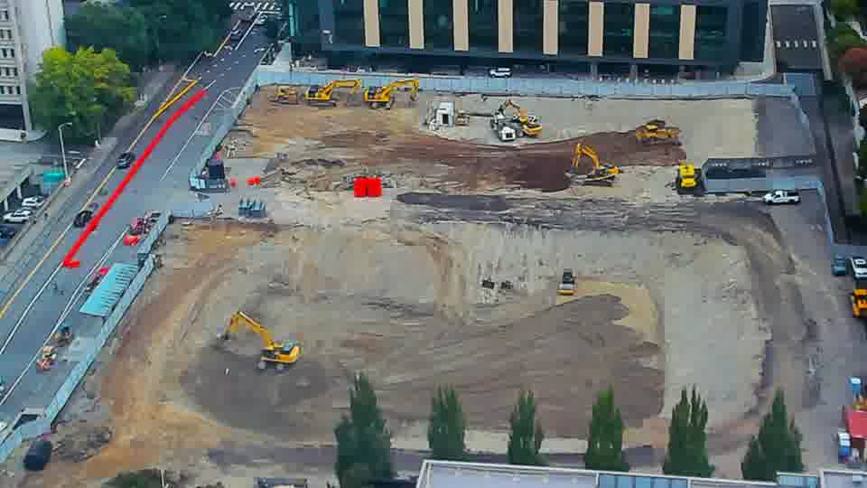 Construction camera frame at 8:15 AM PT. A vehicle has entered the site from the driveway on the left side of the frame.