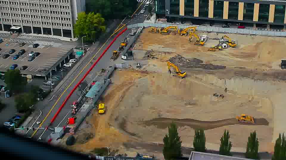 Construction camera frame at 2:00 PM PT. A yellow vehicle has appeared on the left side of the site, near the street. Otherwise, no visible change between these frames.