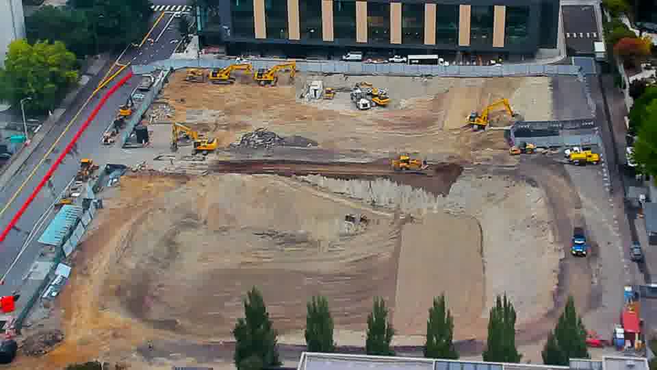 Construction camera frame at 7:15 AM PT. A small blue vehicle has appeared near the center of the site.