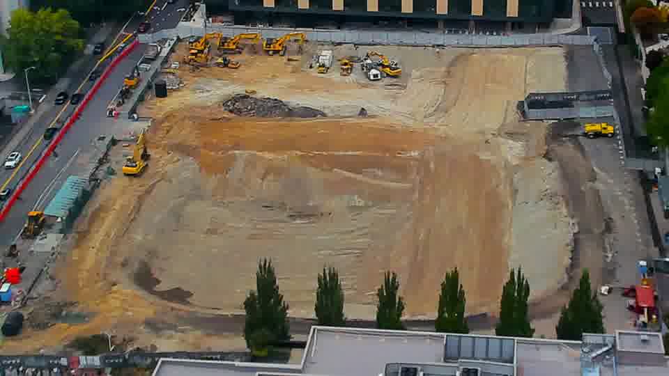 Construction camera frame at 2:30 PM PT. A yellow dump truck has entered the site via the driveway on the left side of the frame.