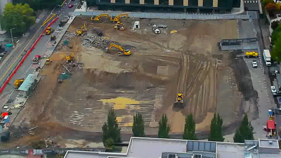 Construction camera frame at 1:15 PM PT. A yellow machine has moved from the center of the site to the lower right corner. Otherwise, no visible change between these frames.