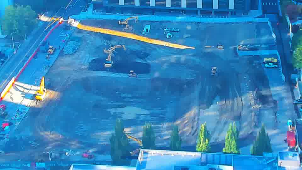 Construction camera frame at 8:45 AM PT. A yellow machine has moved slightly within the site, shifting its position near the center of the frame.